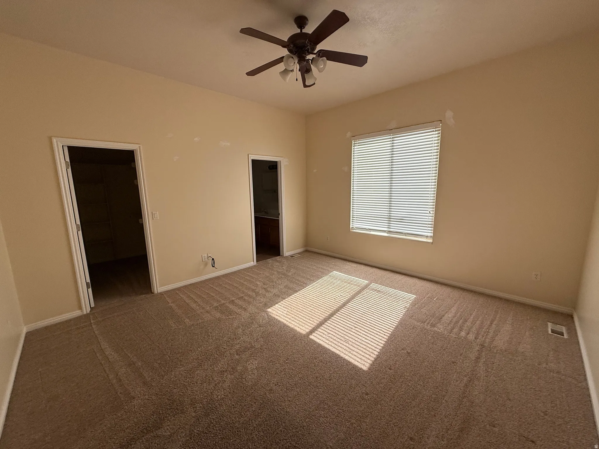 Carpeted room featuring a ceiling fan with light fixture, a window with horizontal blinds, and two doorways