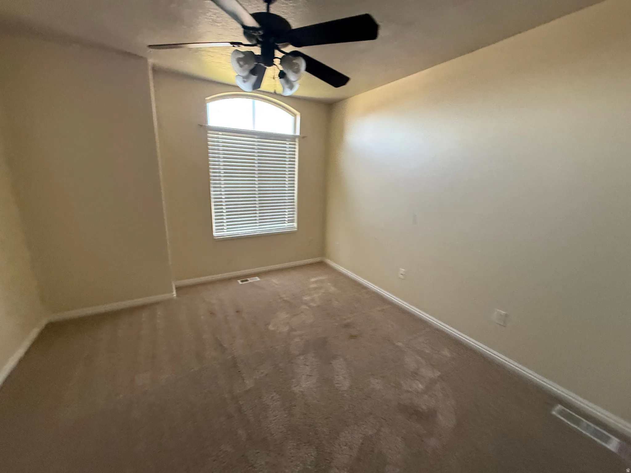 Room featuring a high arched window with horizontal blinds, neutral wall paint, and a ceiling fan with integrated lighting