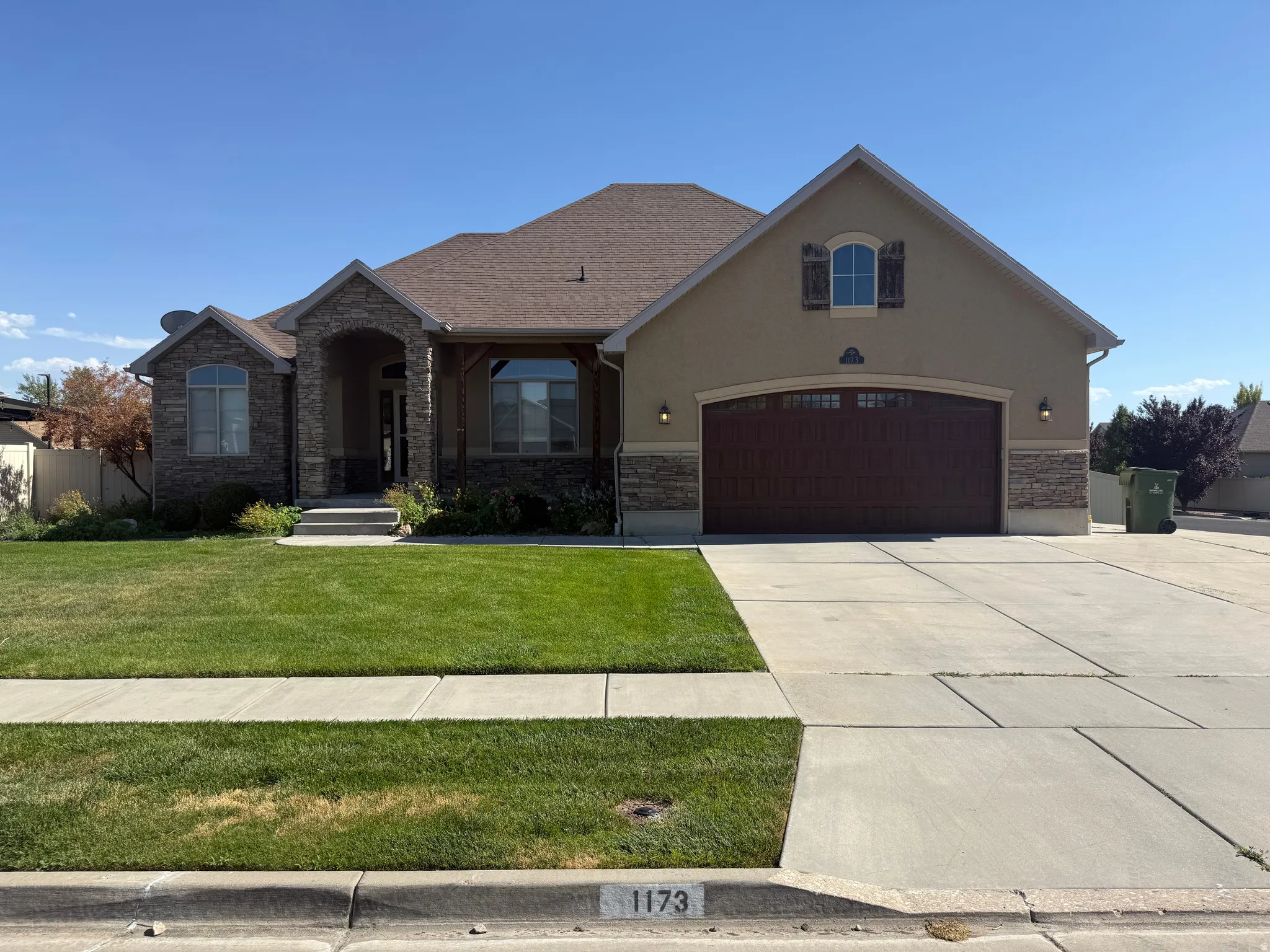 Ranch-style residence featuring a prominent stone and stucco facade, an arched entry, and a large wood-finish garage door
