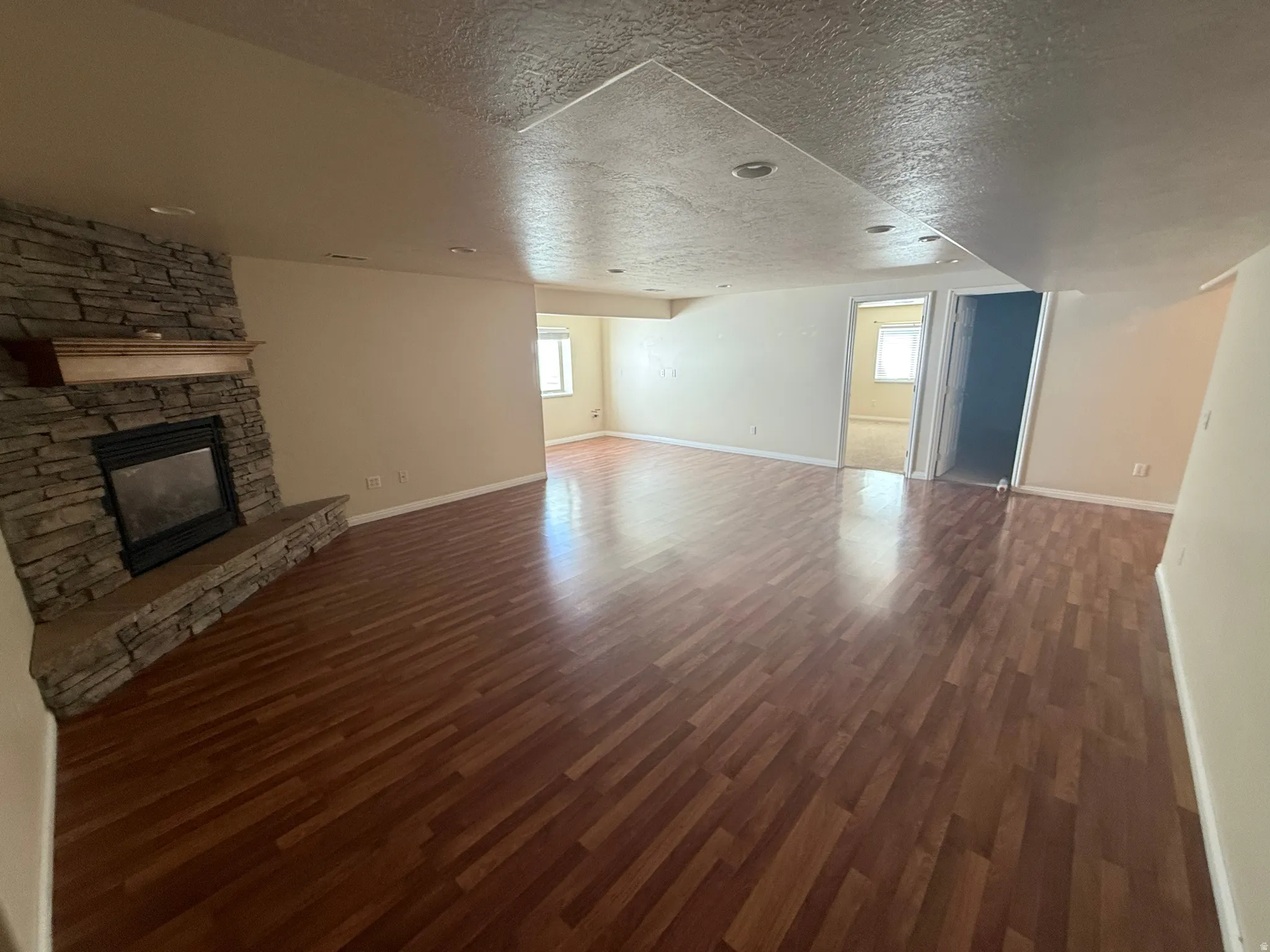 Spacious living area featuring wood-finish flooring, a stacked stone fireplace with a substantial hearth and wood mantle, recessed lighting, and neutral wall paint