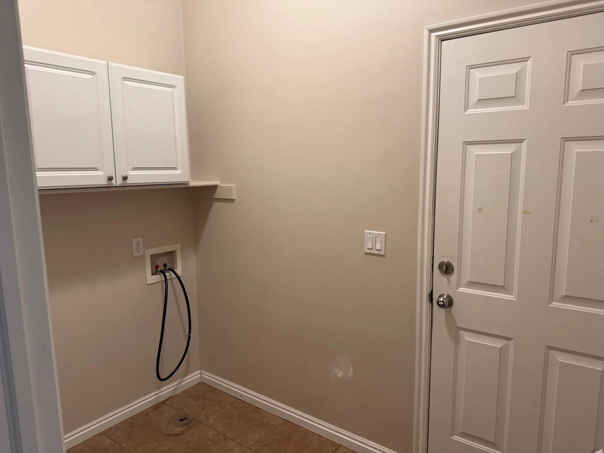 Laundry area featuring two white upper cabinets, a built-in shelf, and a tiled floor