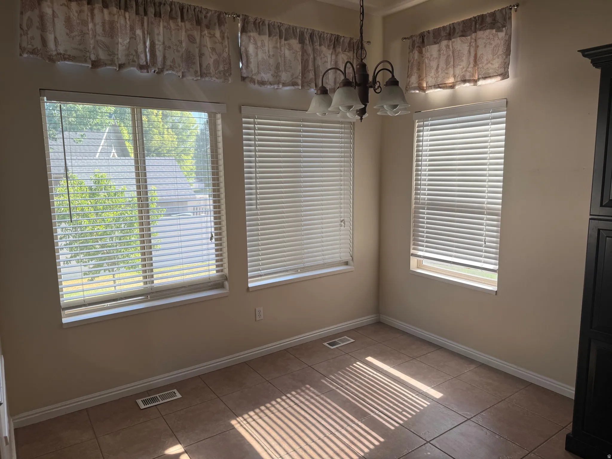 Room featuring three windows with horizontal blinds, a ceiling-mounted light fixture, tile flooring, and a built-in dark wood cabinet