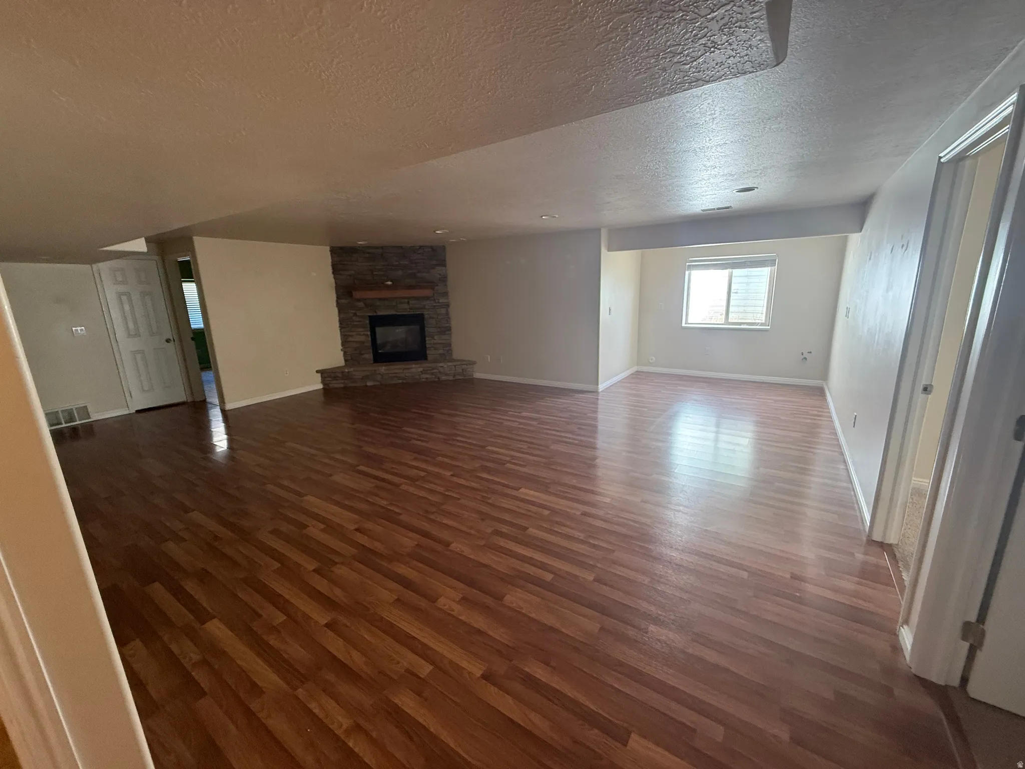 Spacious interior featuring wood-finish flooring, a stone-clad fireplace with a wood mantle, neutral wall tones, and a window with blinds