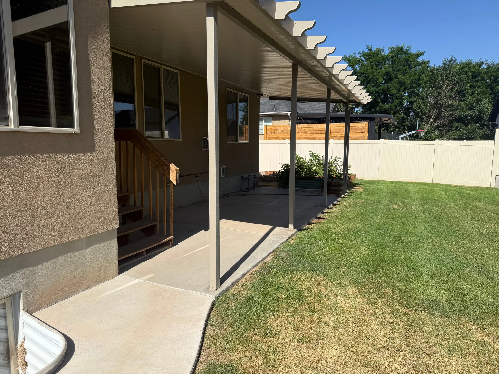 Expansive backyard featuring a covered patio with decorative lattice accents, a concrete walkway, a privacy fence, and a generous lawn area
