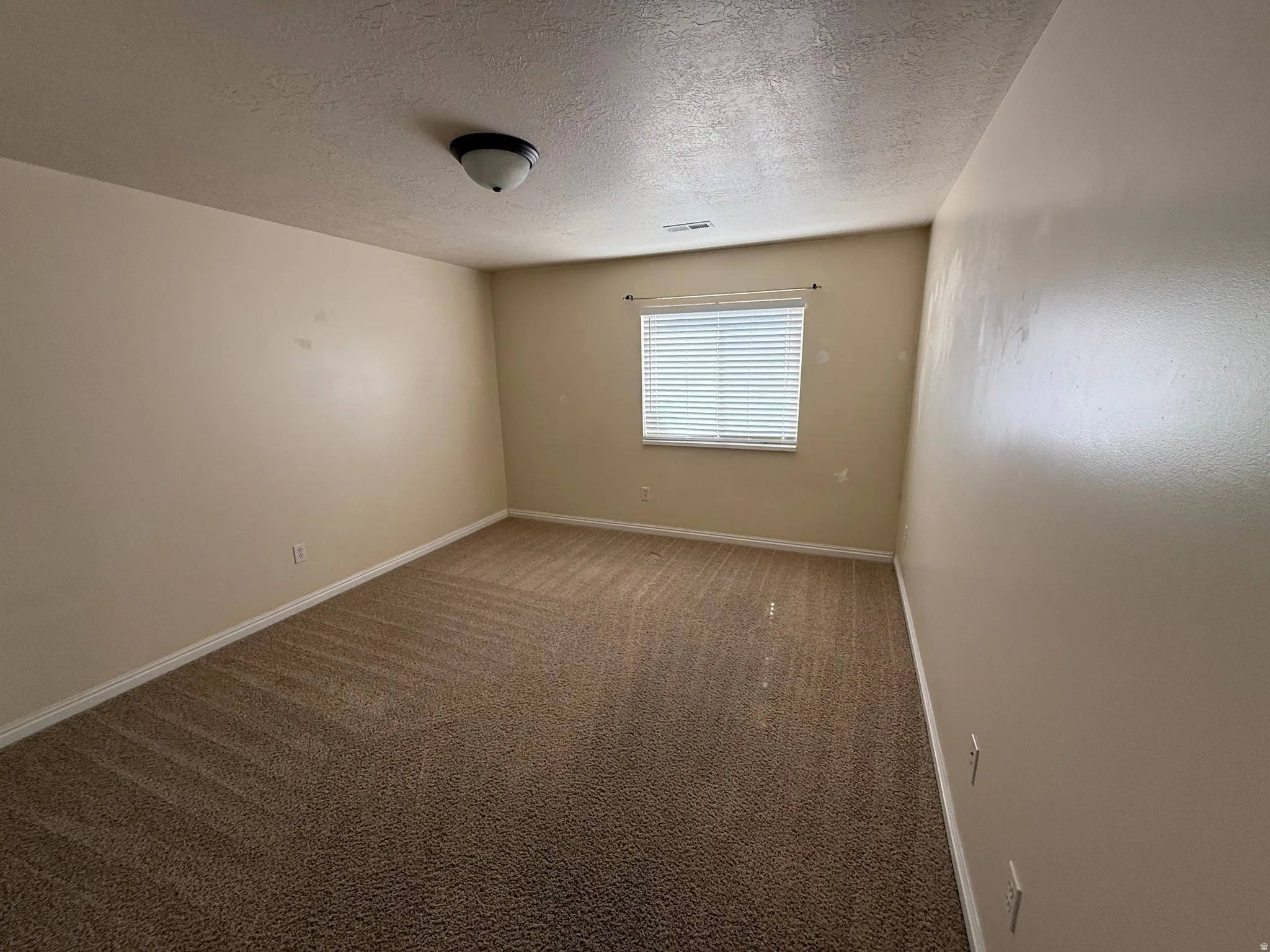 Spacious room featuring neutral-toned walls, a single window with blinds, and a flush-mount ceiling light