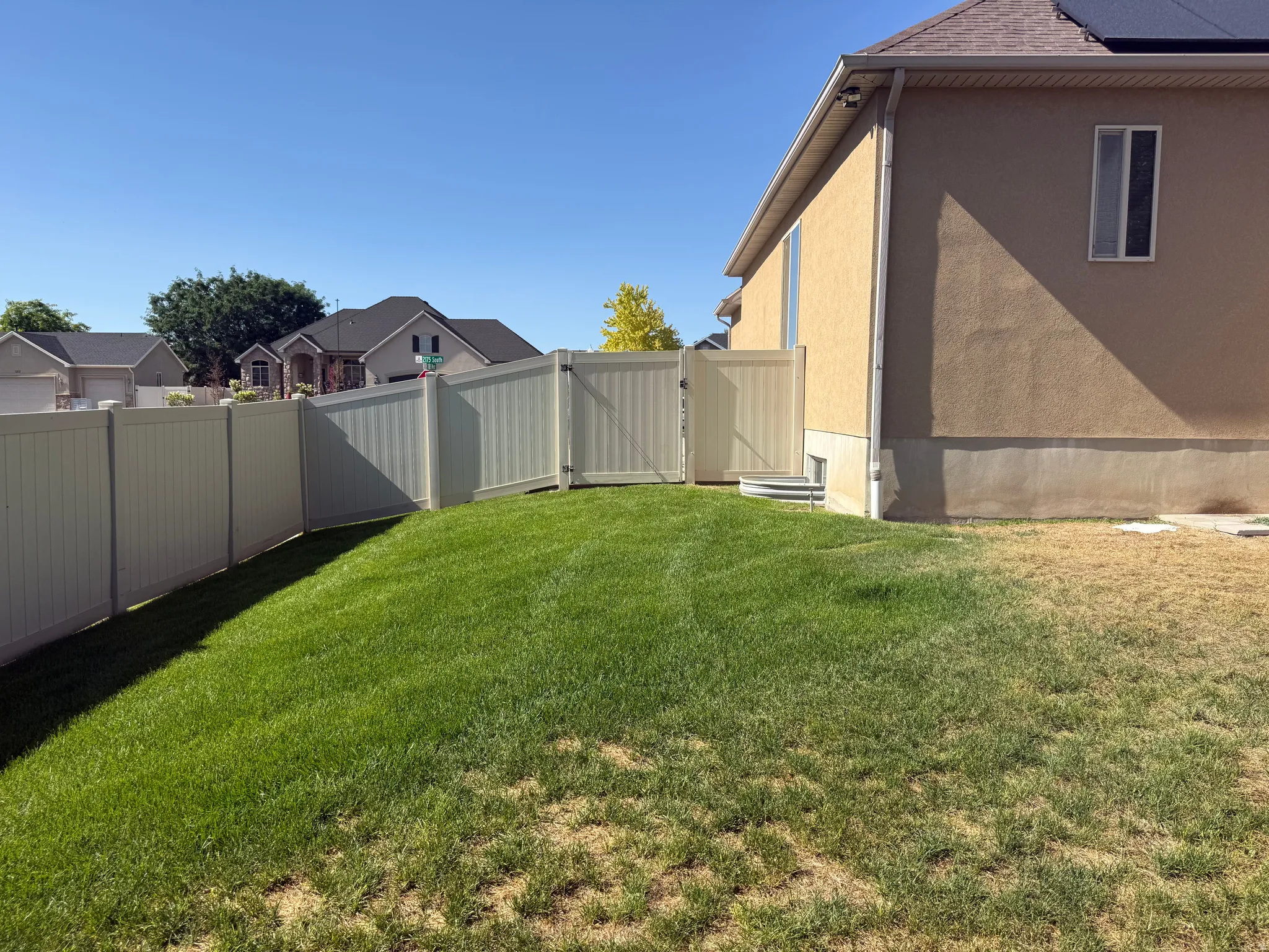Fenced backyard featuring a manicured lawn, vinyl privacy fencing with gate, and stucco exterior