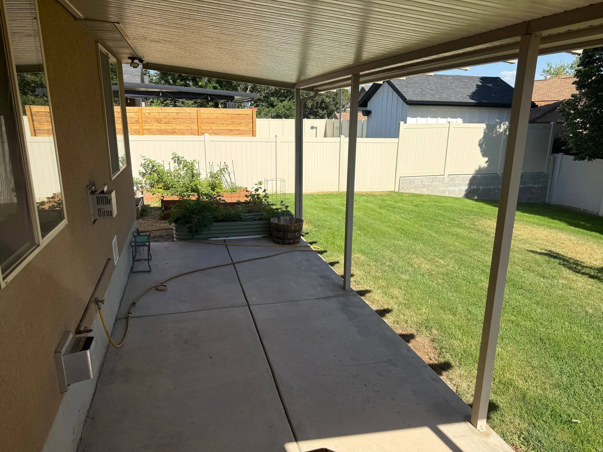 Covered patio with concrete flooring, bordered by a manicured lawn and privacy fencing