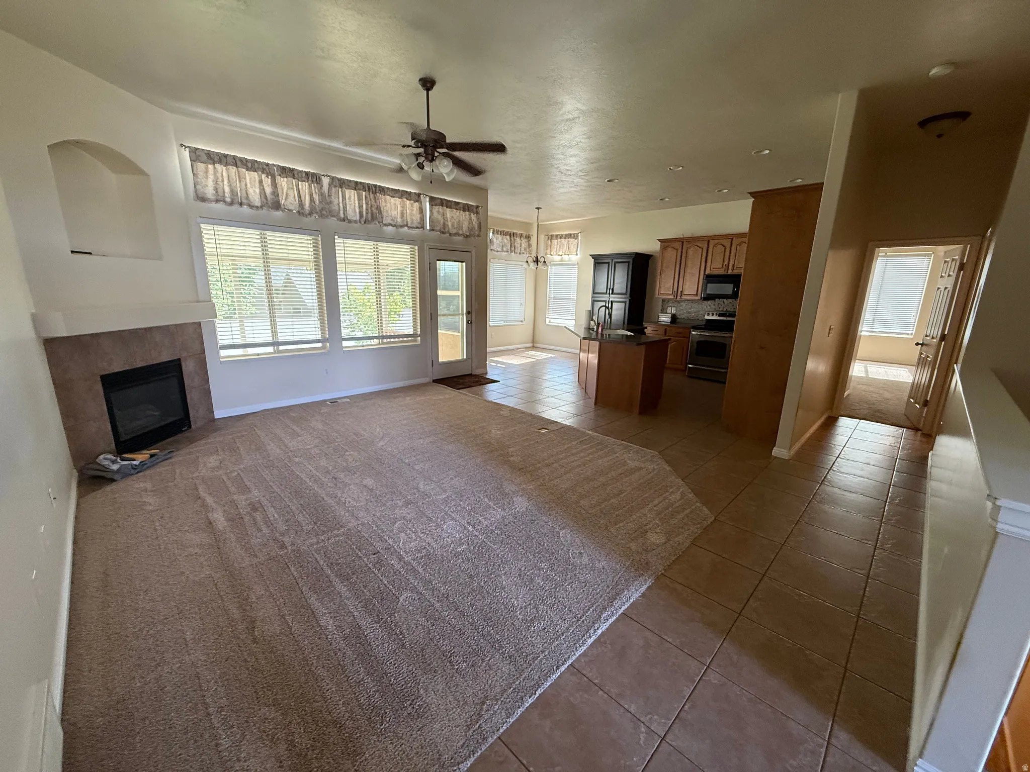 Open-concept living space featuring a fireplace with a tiled surround and mantel, expansive windows, a ceiling fan, and a kitchen with wood cabinetry and tile flooring