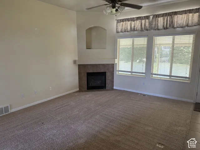 Living area featuring an integrated fireplace with a tile surround and mantel, two large windows with horizontal blinds, a ceiling fan with integrated lighting, and a neutral carpet