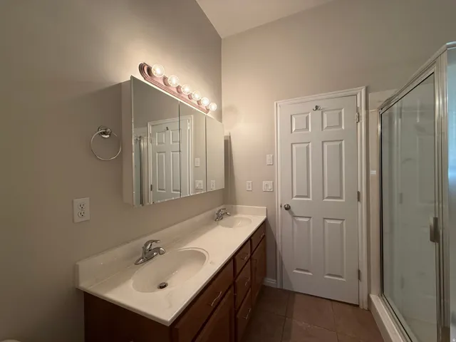 Dual vanity with integrated sinks, wood-finish cabinetry, and an overhead mirror with task lighting
