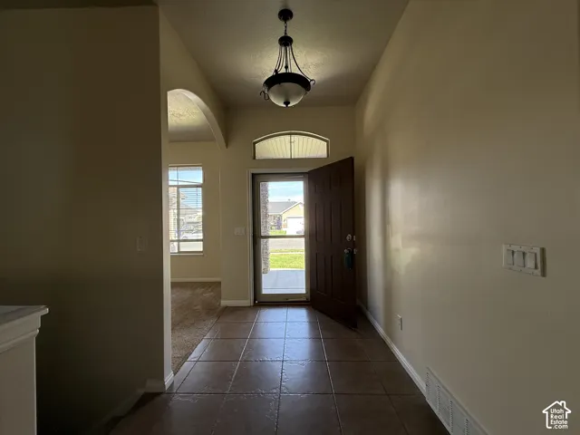 Tiled entryway featuring a decorative light fixture, arched doorway, and transom window above the front door