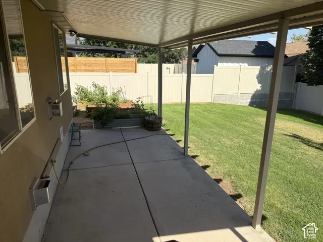 Covered patio with concrete flooring, bordered by a manicured lawn and privacy fencing