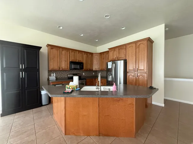 Kitchen featuring a large central island with an integrated sink, wood-finish cabinetry, a mosaic tile backsplash, and recessed lighting
