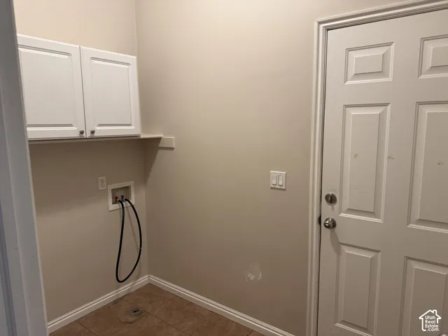 Laundry area featuring two whiteupper cabinets, a built-in shelf, and a tiled floor