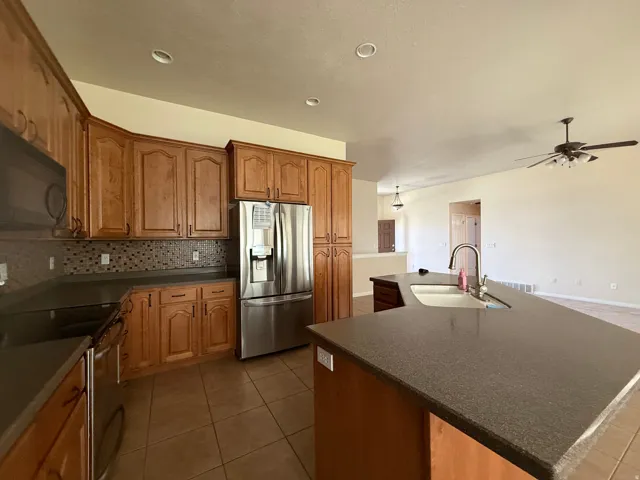 Kitchen with wood cabinetry, dark countertops, tiled backsplash, stainless steel appliances, and a kitchen island with an undermount sink