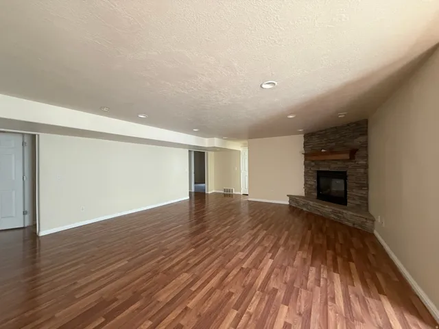 Wood-finish flooring throughout, recessed ceiling lighting, stone-clad fireplace with wood mantel, and neutral wall tones