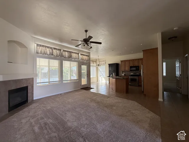 Living area with an integrated kitchen, featuring a ceiling fan, a tiled fireplace with a mantel, and multiple windows