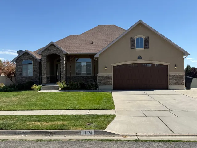 Ranch-style residence featuring a stucco and stone facade, arched entryway, and an attached two-car garage with a wood-finish door