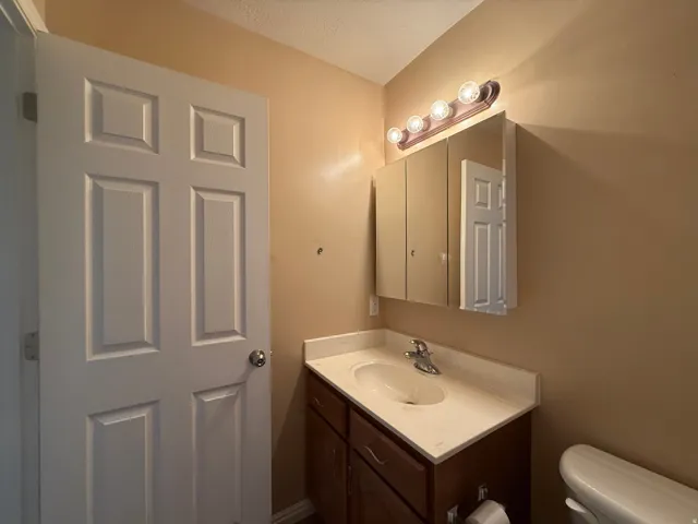 White four-panel interior door, single-sink vanity with white countertop, chrome faucet, medicine cabinet with mirrored door, and five-bulb vanity light fixture