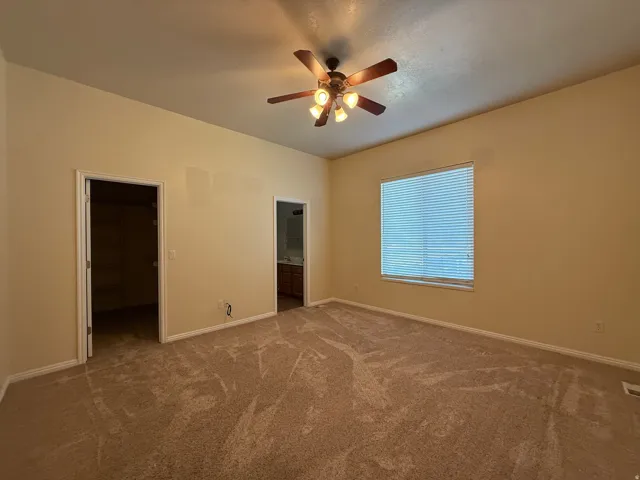 Carpeted interior space featuring a window with blinds, ceiling fan with light fixture, and two doorways