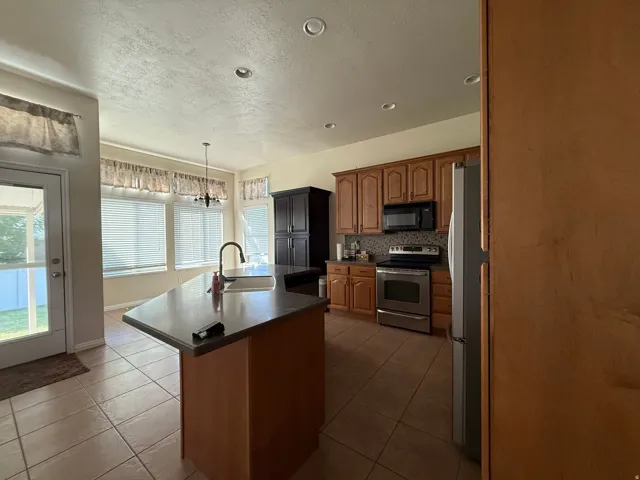 Kitchen featuring recessed lighting, a central island with a sink, wood cabinetry, stainless steel appliances, and tile flooring