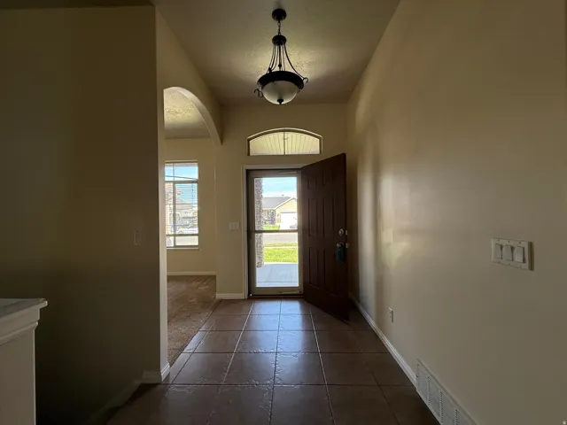 Tiled entryway featuring a decorative light fixture, arched doorway, and transom window above the front door