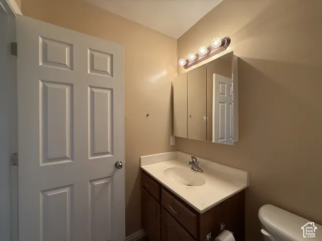 White four-panel interior door, single-sink vanity with white countertop, chrome faucet, medicine cabinet with mirrored door, and five-bulb vanity light fixture