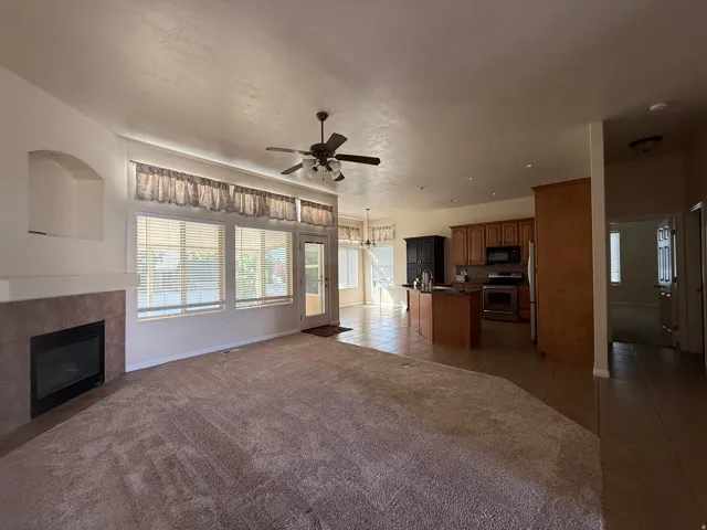 Living area with an integrated kitchen, featuring a ceiling fan, a tiled fireplace with a mantel, and multiple windows