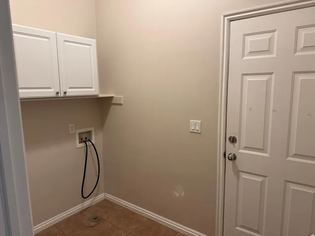 Laundry area featuring two white upper cabinets, a built-in shelf, and a tiled floor