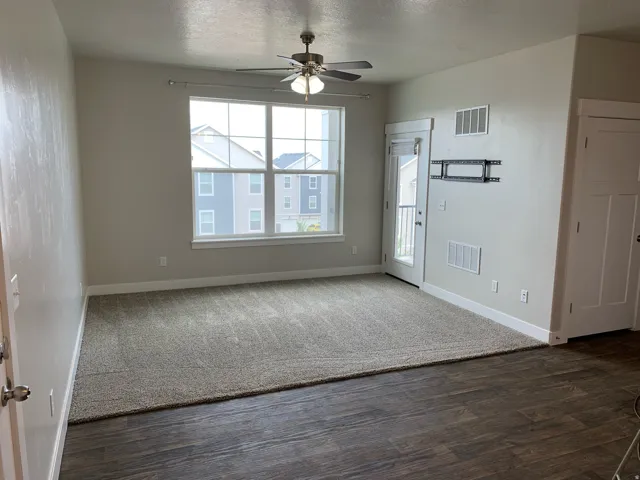 Spacious living area featuring a large window, a ceiling fan with integrated lighting, wood-finish flooring, and a glass-paneled door