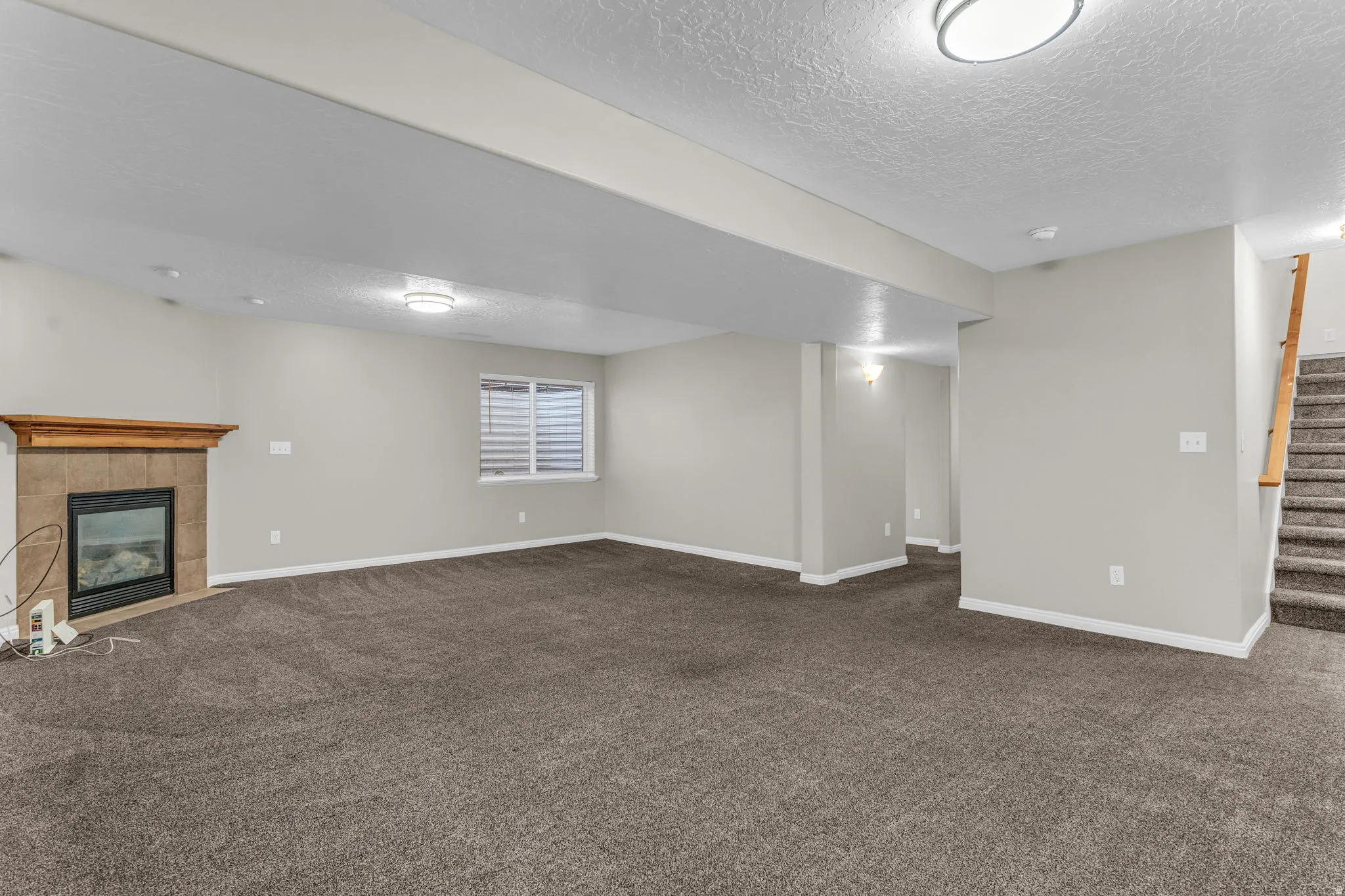 Spacious finished room featuring neutral paint, textured carpet, a fireplace with a wood mantle and tile surround, and recessed lighting