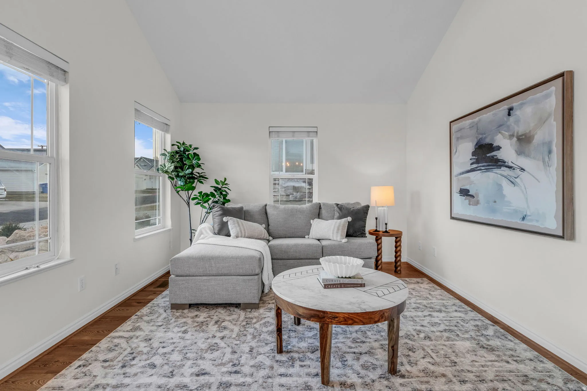 Bright living space featuring vaulted ceilings, multiple windows, wood-finish flooring, and crisp white walls