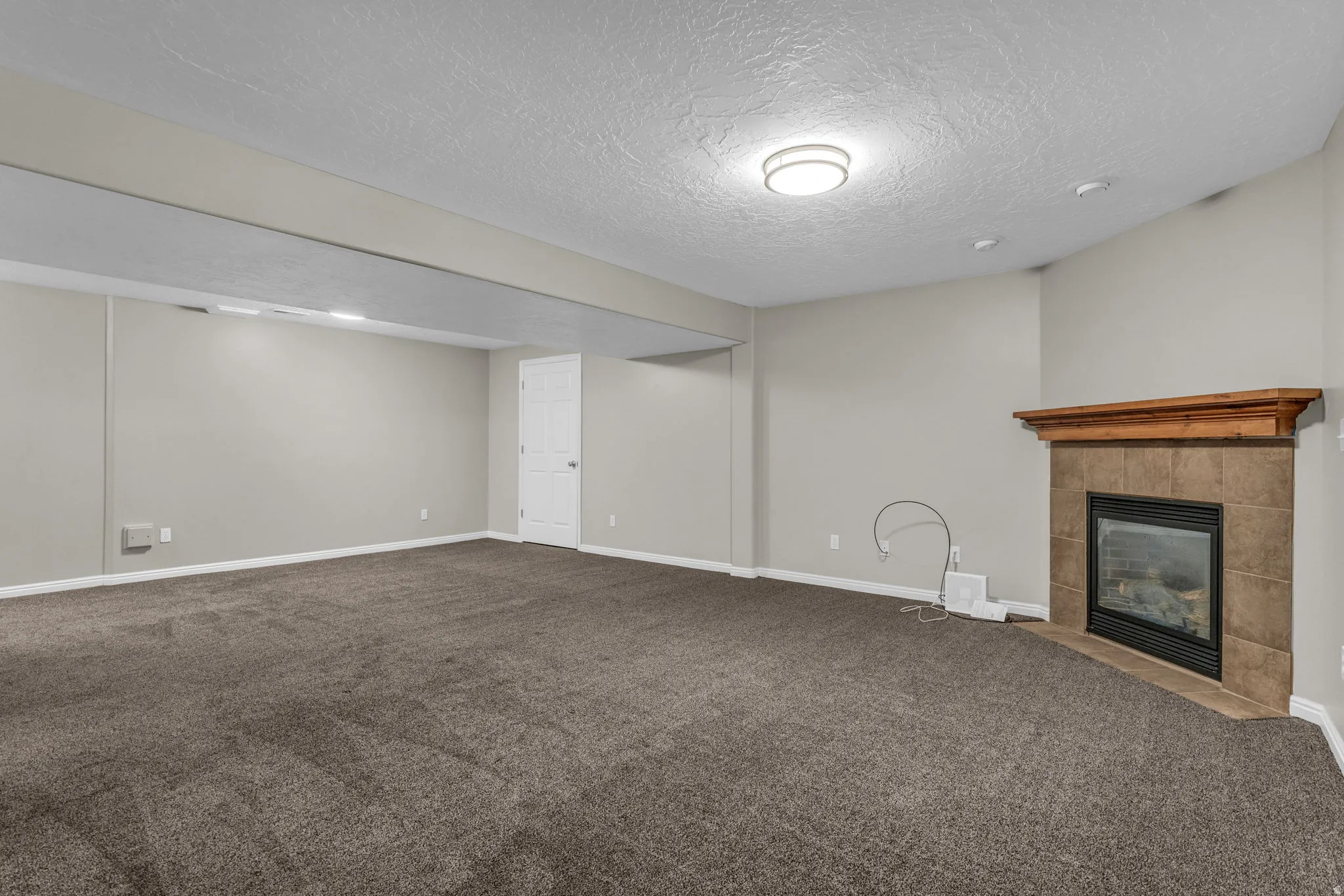 Spacious interior featuring neutral wall tones, textured ceiling, recessed lighting, and a built-in fireplace with a tile surround and wood mantel