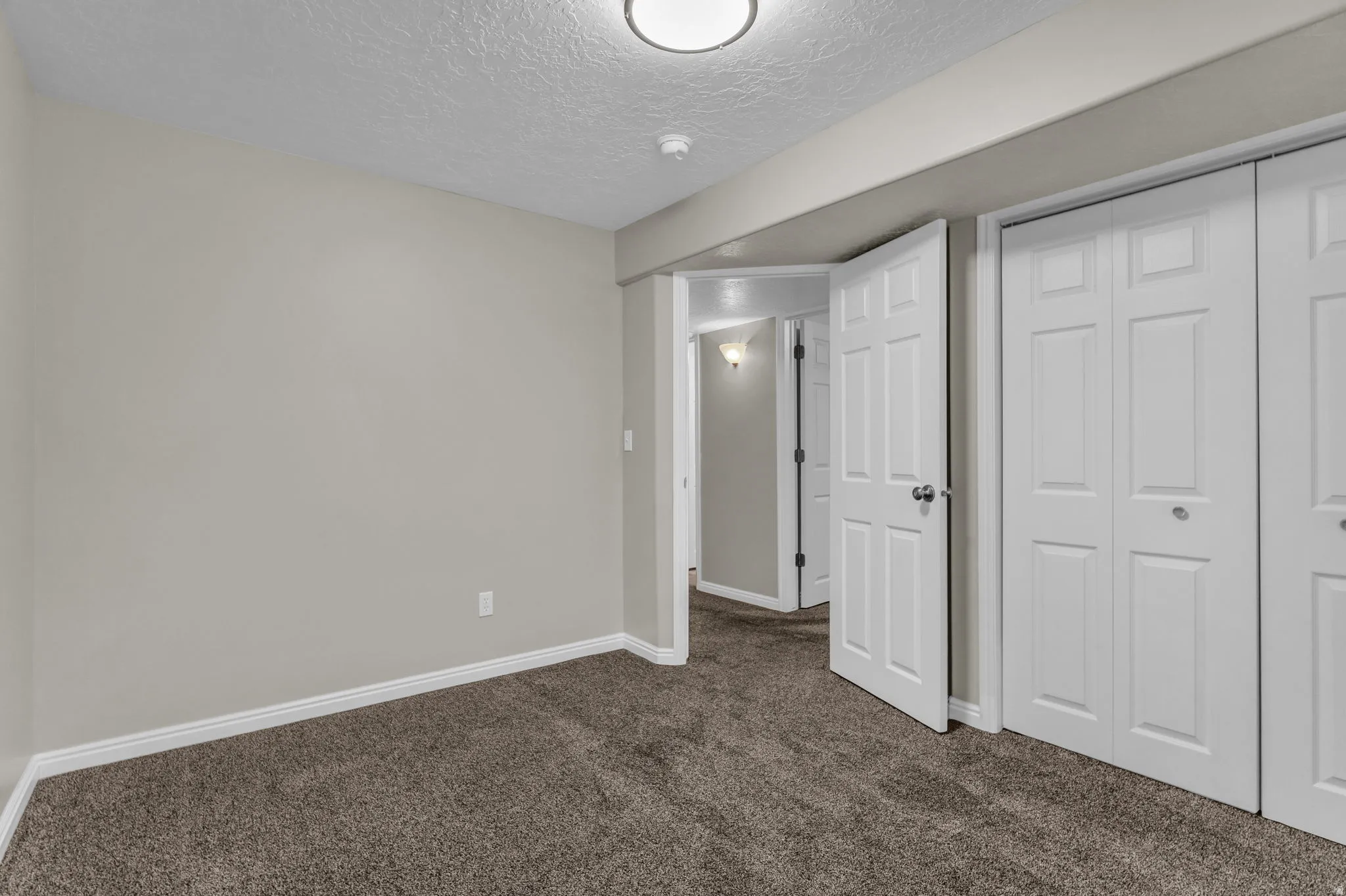 Neutral-toned room with plush carpet flooring, white baseboards, and a flush-mount ceiling light