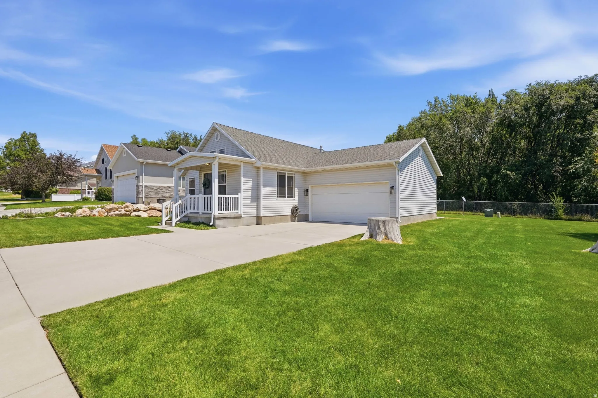 Ranch-style residence featuring light-colored siding, an attached two-car garage, and a covered porch with white railings