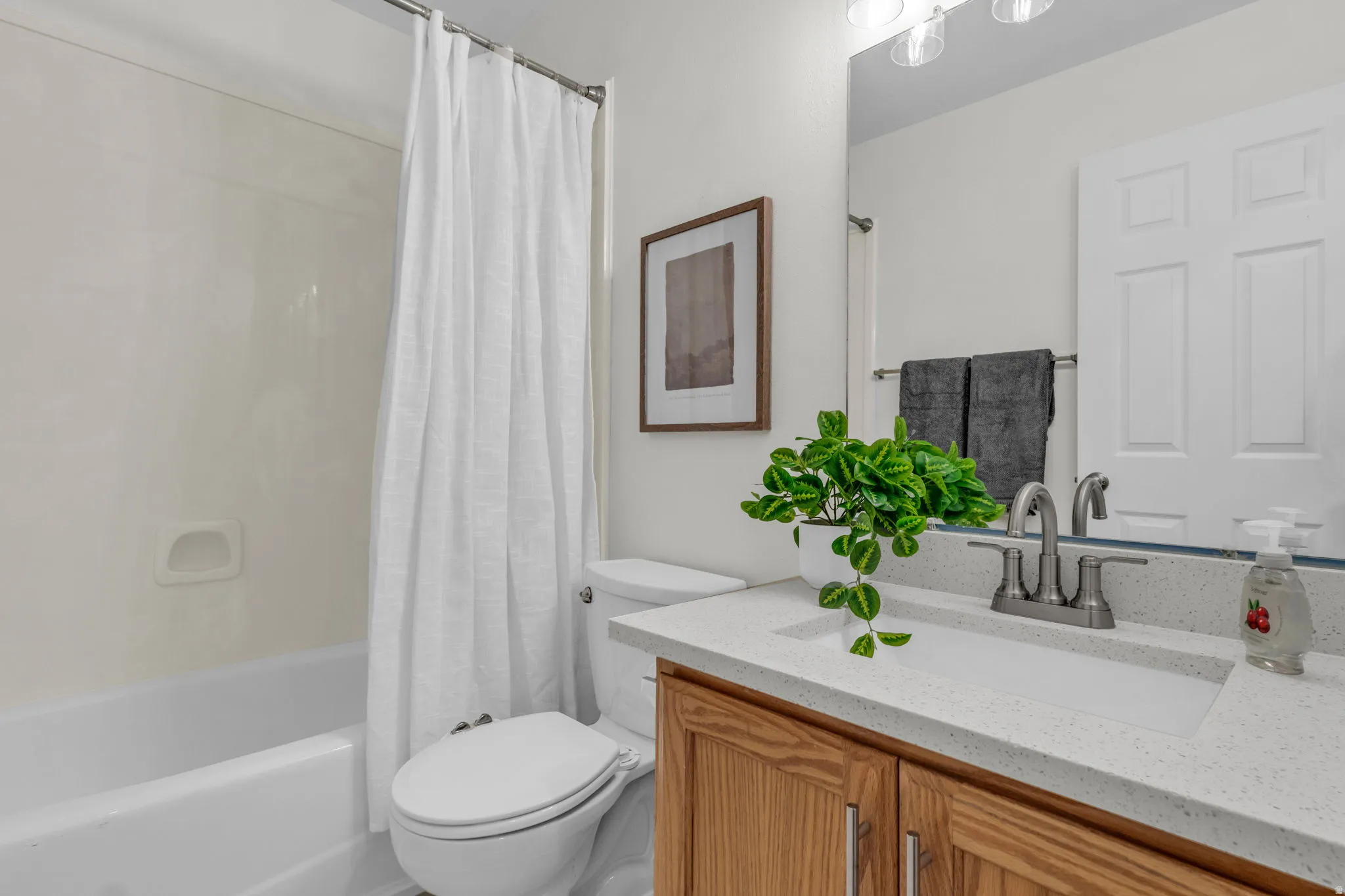 Bathroom featuring a white tub with shower, toilet, and a wood-finish vanity with a light-colored countertop and integrated sink