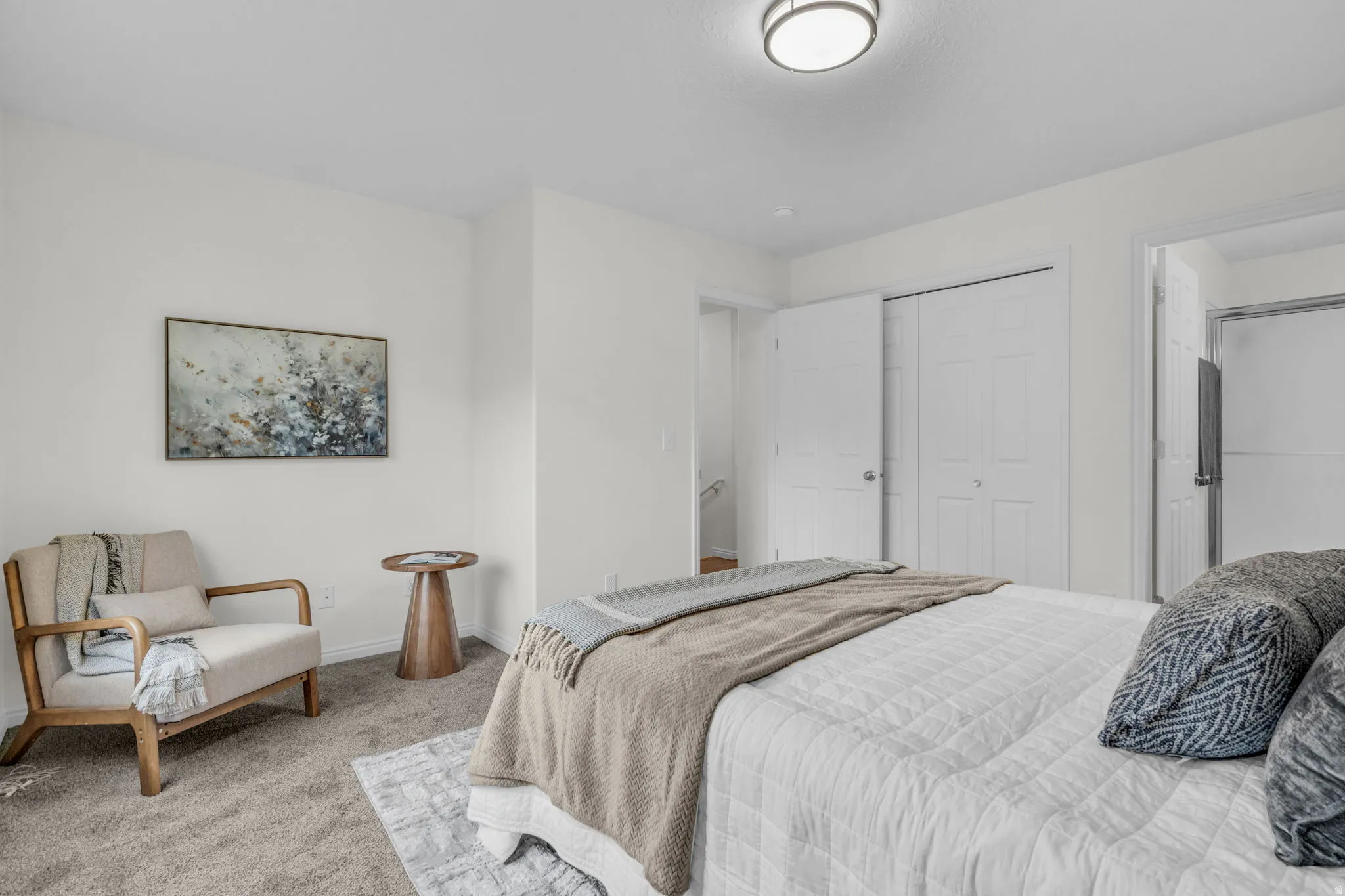 Carpeted bedroom featuring white walls, a flush-mount ceiling light fixture, bi-fold closet doors, and an open doorway to a bathroom with a glass-enclosed shower