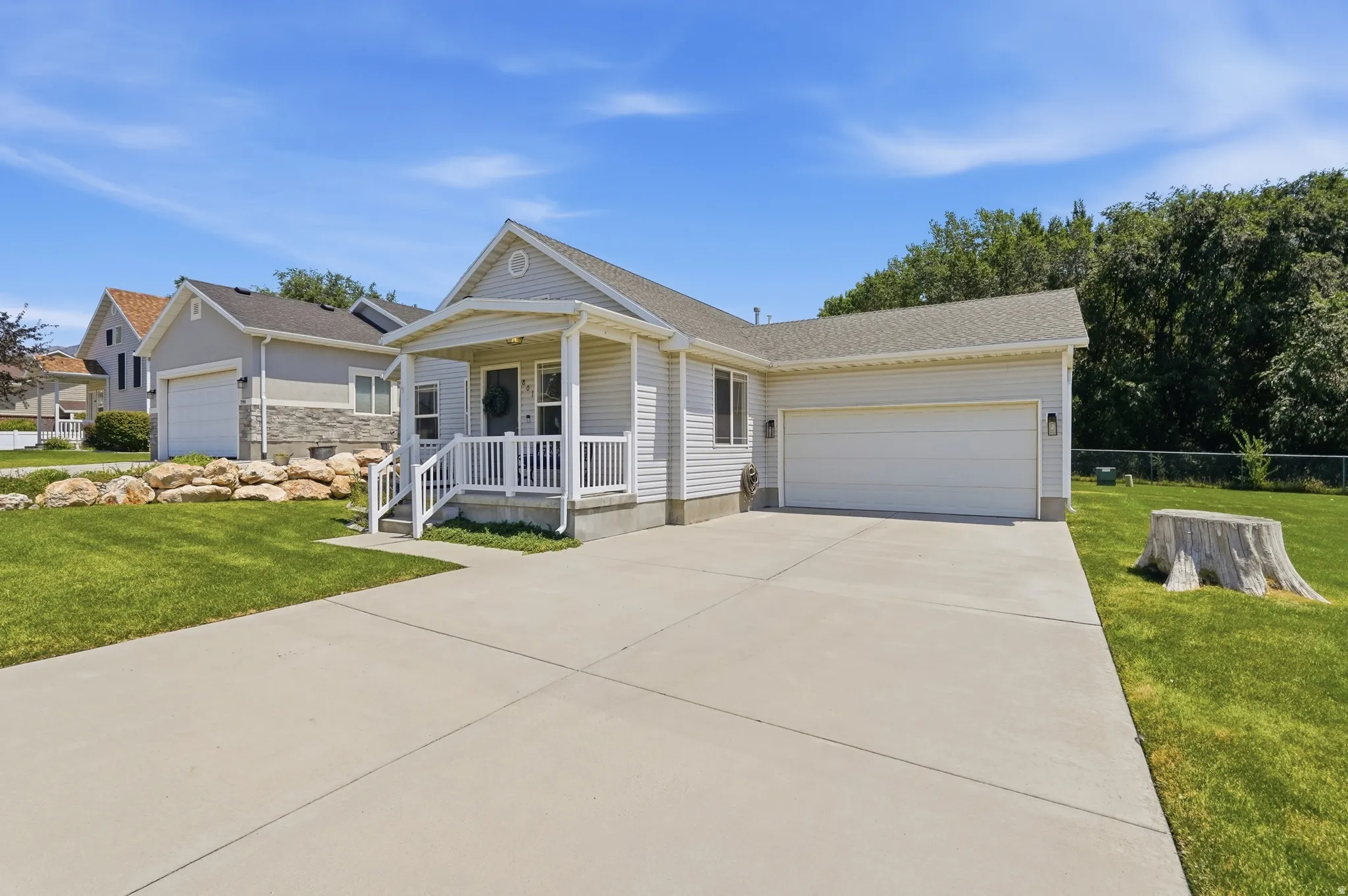 Ranch-style residence featuring light-colored siding, an attached garage, a covered front porch with white railings, a concrete driveway, and a manicured lawn