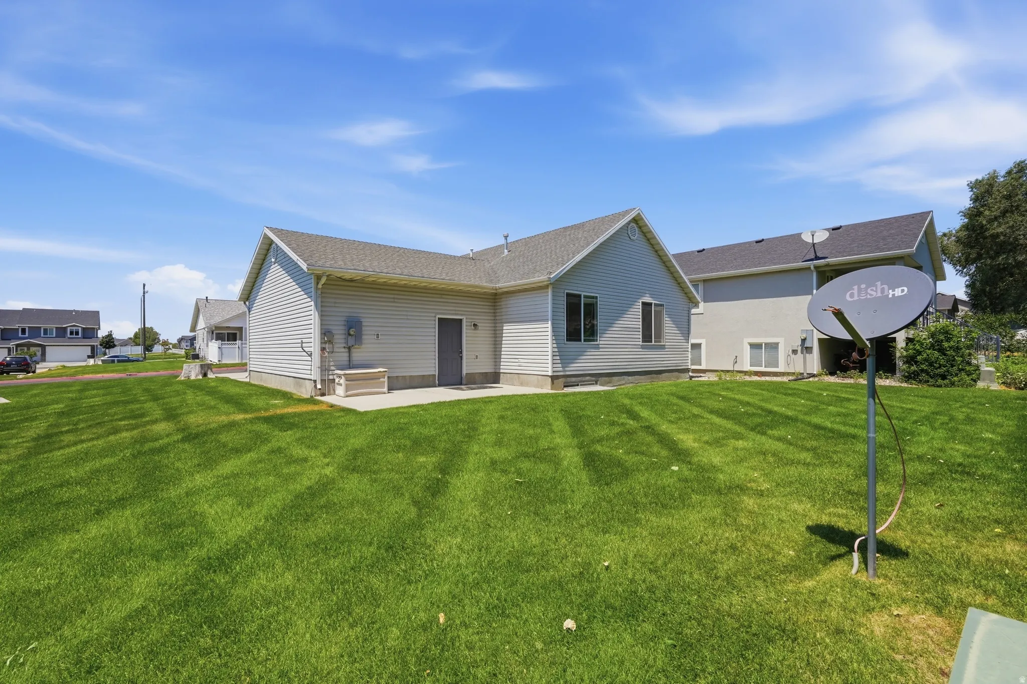 Spacious backyard featuring a manicured lawn, a concrete patio, and a light-colored siding exterior