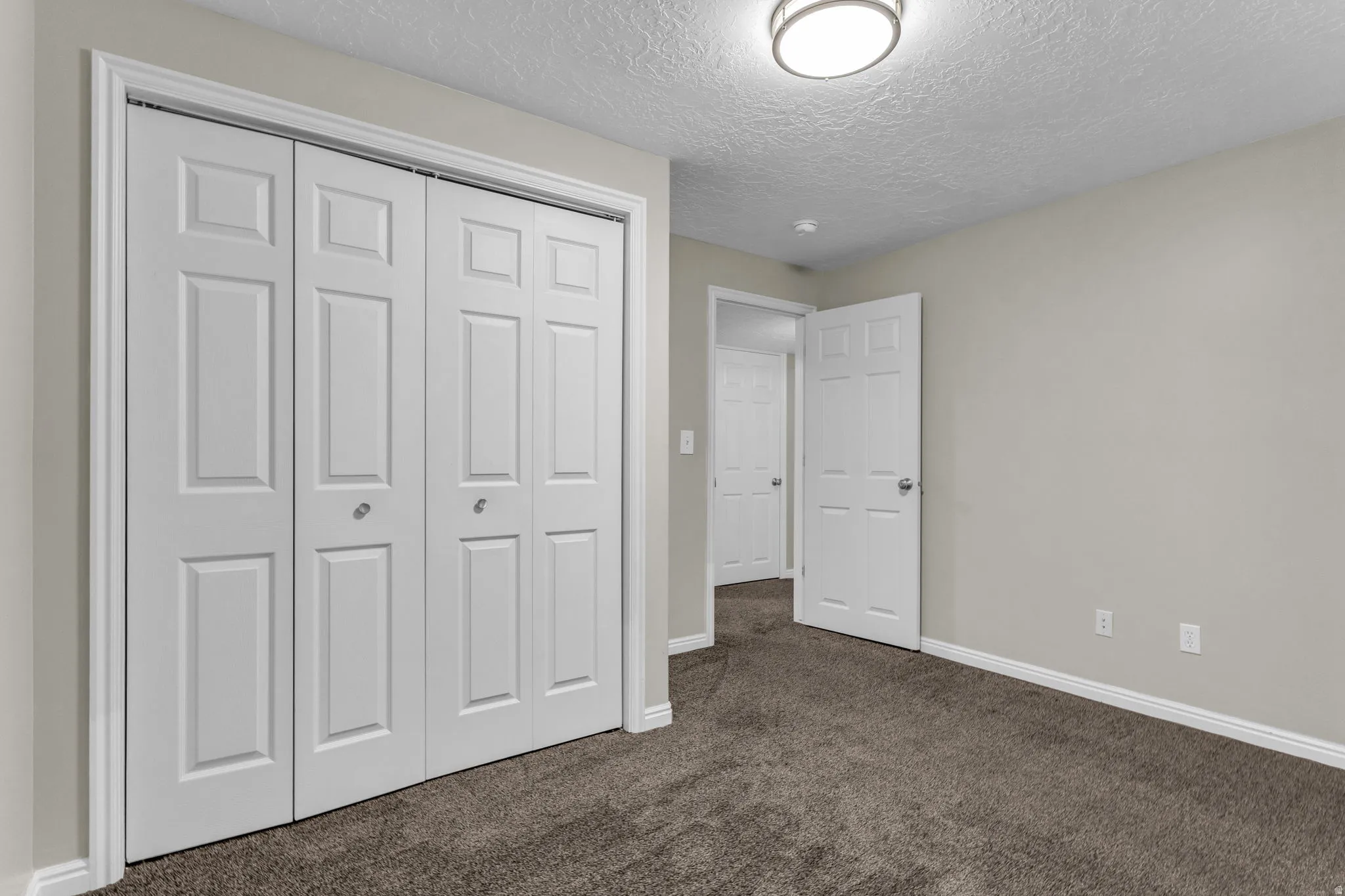 Bedroom featuring bi-fold closet doors, neutral wall paint, and dark textured carpeting