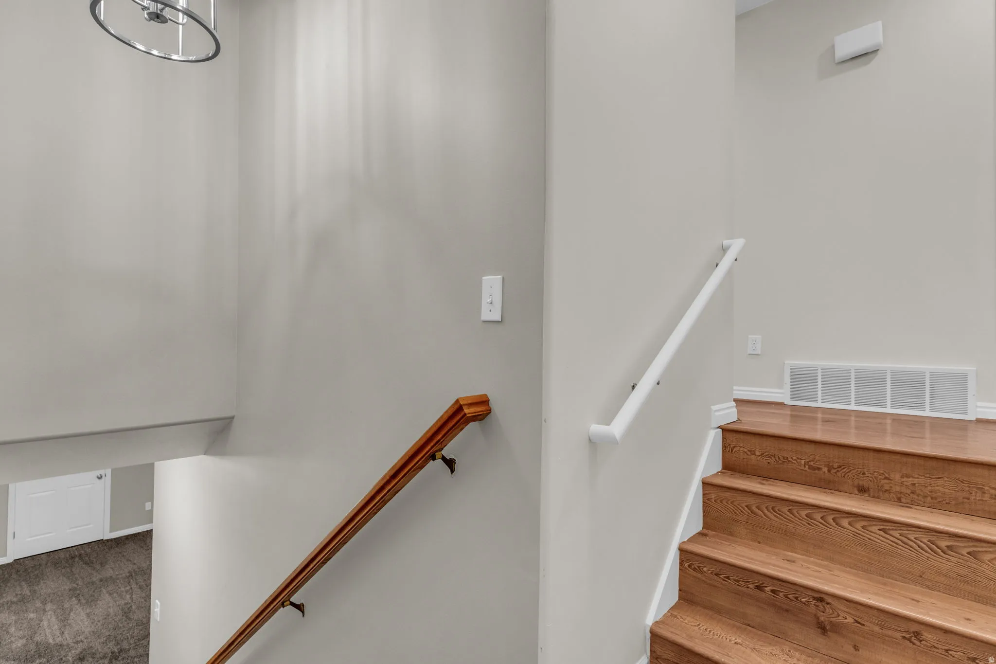 Staircase featuring wood-finish treads and risers, a white handrail, and a contrasting wood-finish handrail