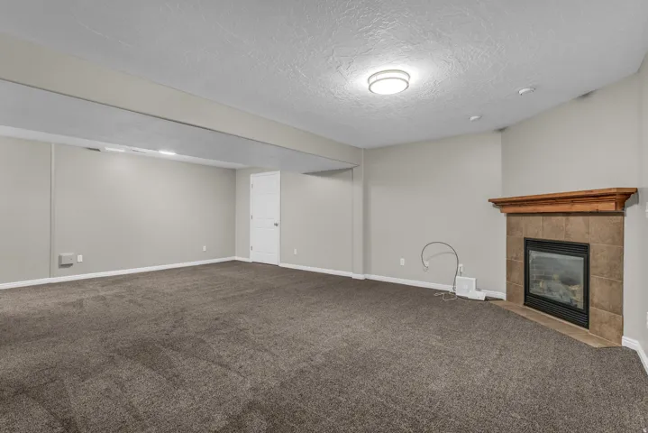 Spacious interior featuring neutral wall tones, textured ceiling, recessed lighting, and a built-in fireplace with a tile surround and wood mantel