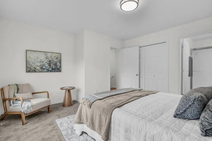 Carpeted bedroom featuring white walls, a flush-mount ceiling light fixture, bi-fold closet doors, and an open doorway to a bathroom with a glass-enclosed shower