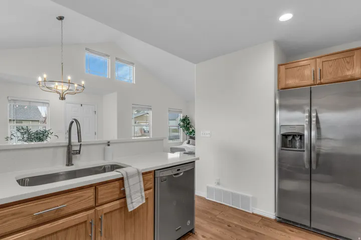 Kitchen featuring wood-finish flooring, stainless steel appliances, light wood cabinetry, and white countertops