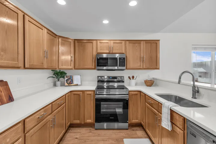 Kitchen featuring wood-finish cabinetry, stainless steel appliances, solid surface countertops, a stainless steel sink with a high-arch faucet, and recessed lighting