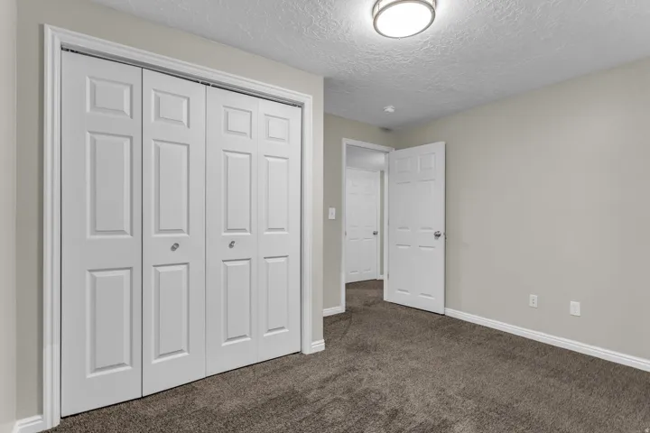 Bedroom featuring bi-fold closet doors, neutral wall paint, and dark textured carpeting
