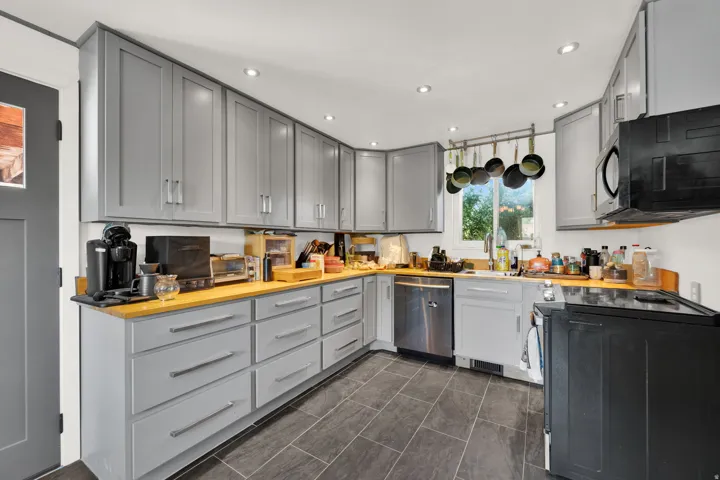 Kitchen featuring light grey cabinetry, wood-finish countertops, stainless steel dishwasher, black electric range, and dark tile flooring