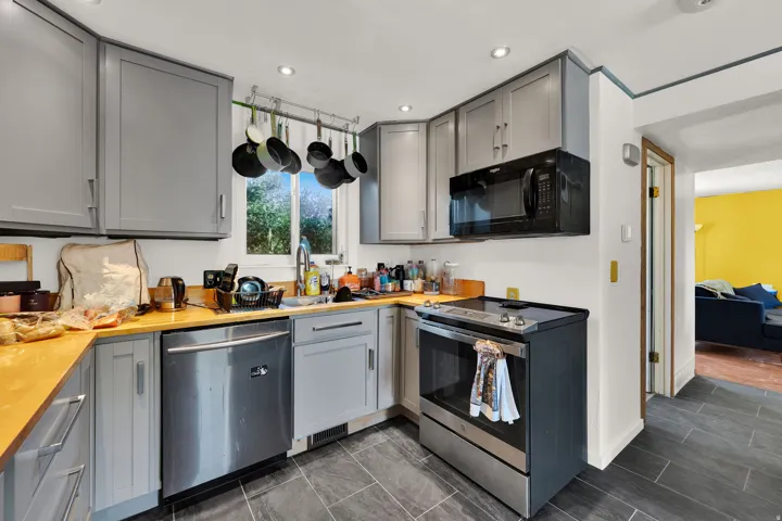 Kitchen featuring grey cabinetry, wood-finish countertops, stainless steel dishwasher, and a black over-the-range microwave