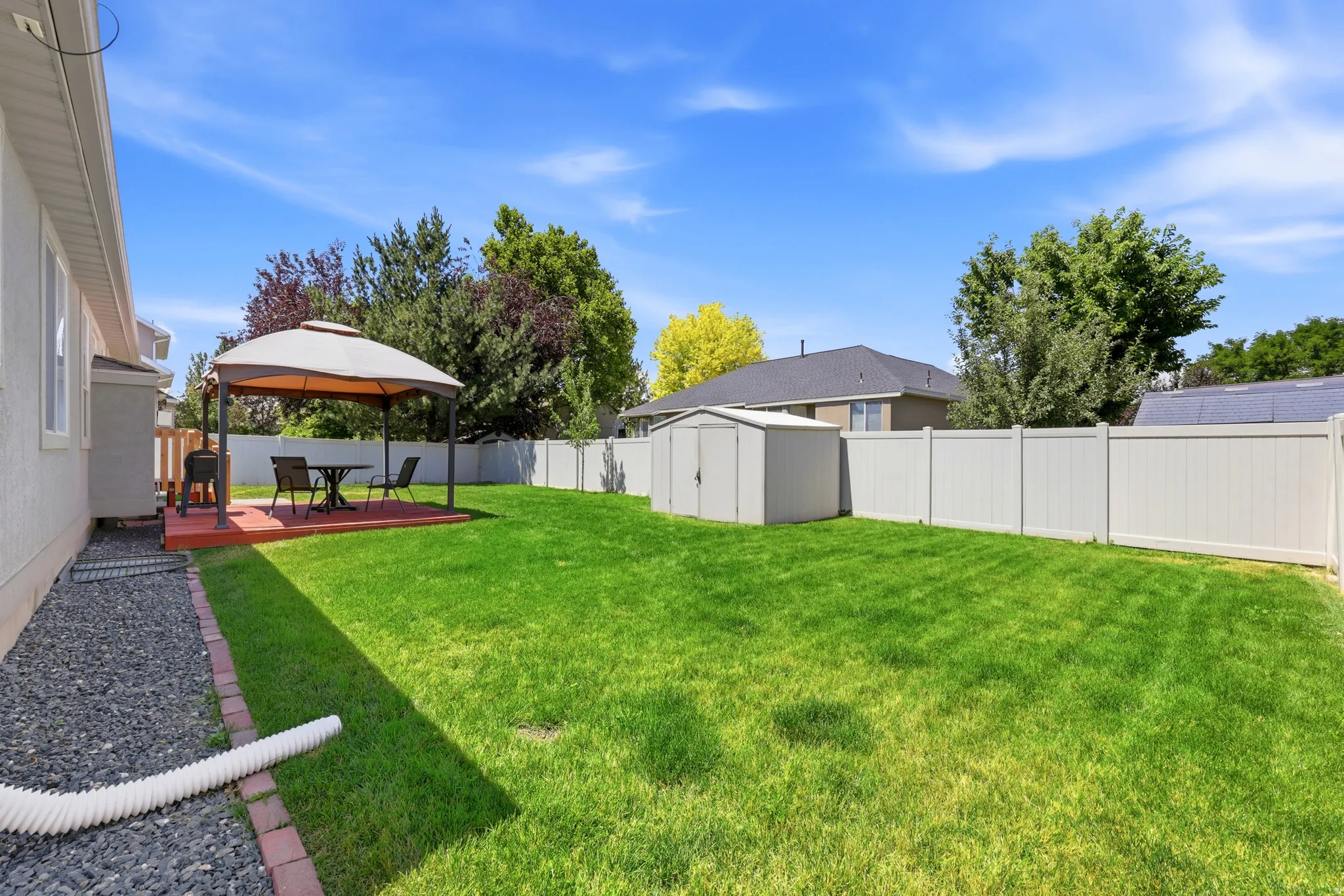 Expansive backyard featuring a green lawn, a raised wooden deck with a gazebo, a storage shed, and a privacy fence