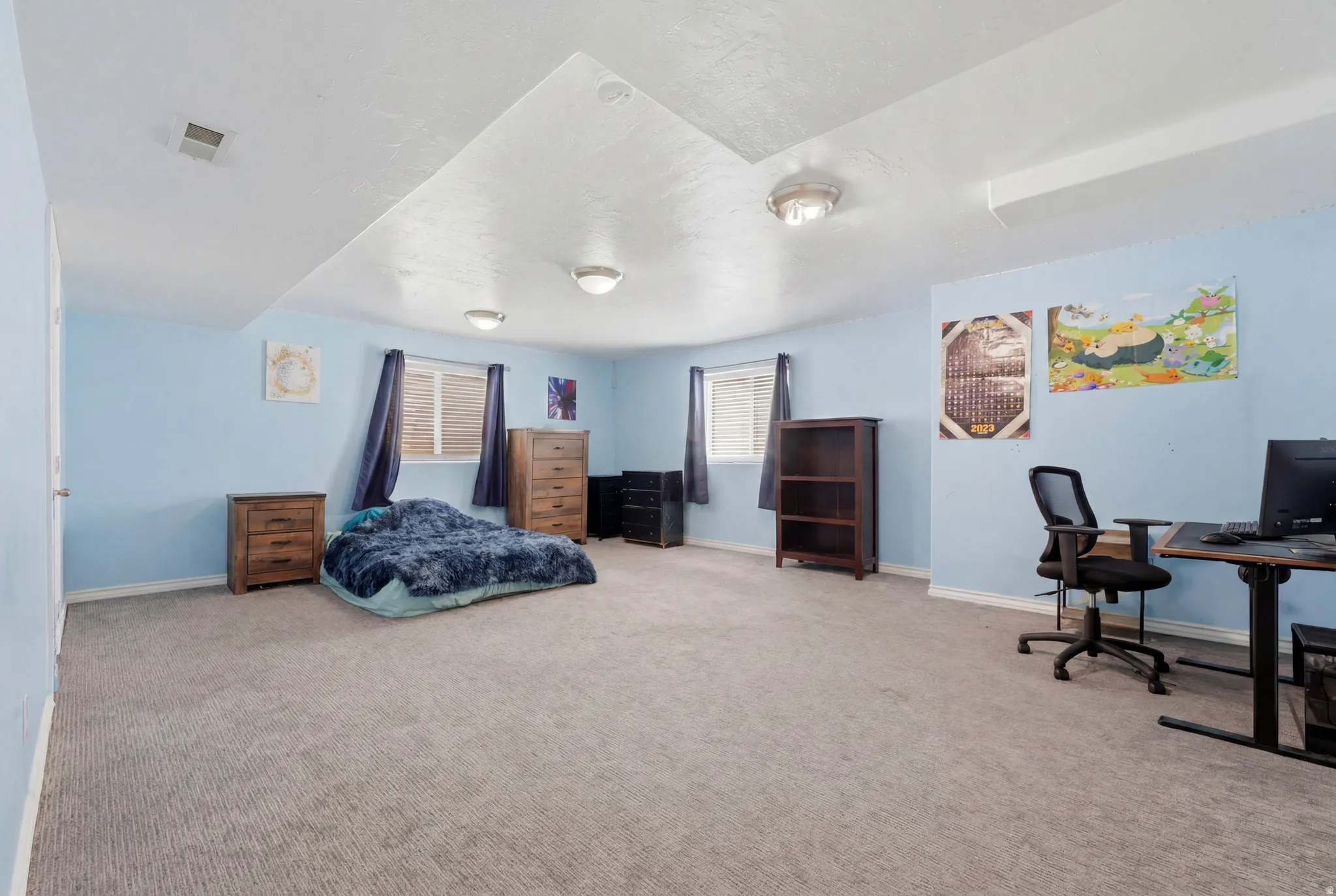 Spacious room featuring light blue walls, gray carpeting, dual windows with blinds, and recessed ceiling lighting